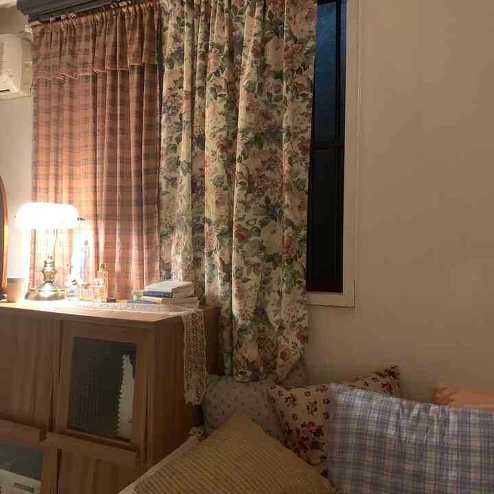 ベージュと花柄のカーテンがある居心地の良いリビング、さまざまなクッションと木製キャビネット、暖かい照明が特徴的なインテリア