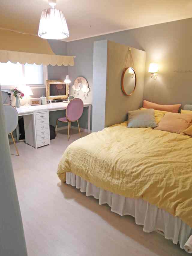 Yellow bedspread and white furniture in a compact bedroom featuring desk, lit table lamp, and round wall mirror in cozy atmosphere