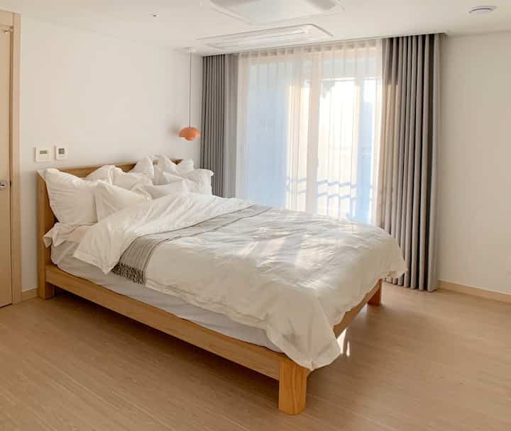 白と木目調が調和したホテルライクなミニマル寝室、ペンダントライトがアクセントとして配置された印象的な空間