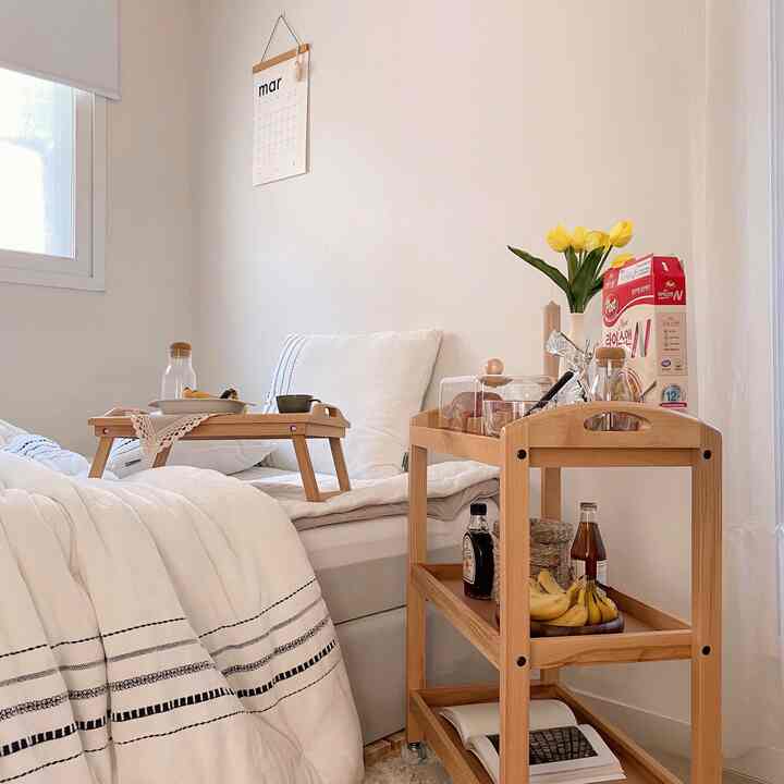 白と木目調が調和した寝室、バーカートとベッドトレイが配置された自然で温かみのあるインテリア