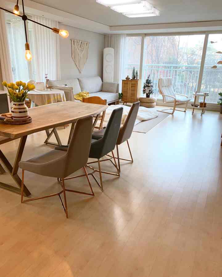 Bright white-toned living room with wood tone dining table and sofa, large window flooding natural light in a natural modern space