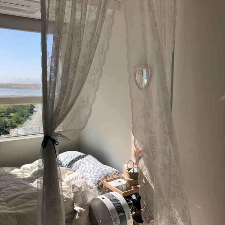 White-toned bedroom filled with natural light, featuring lace curtains and a wooden nightstand creating a cozy ambiance