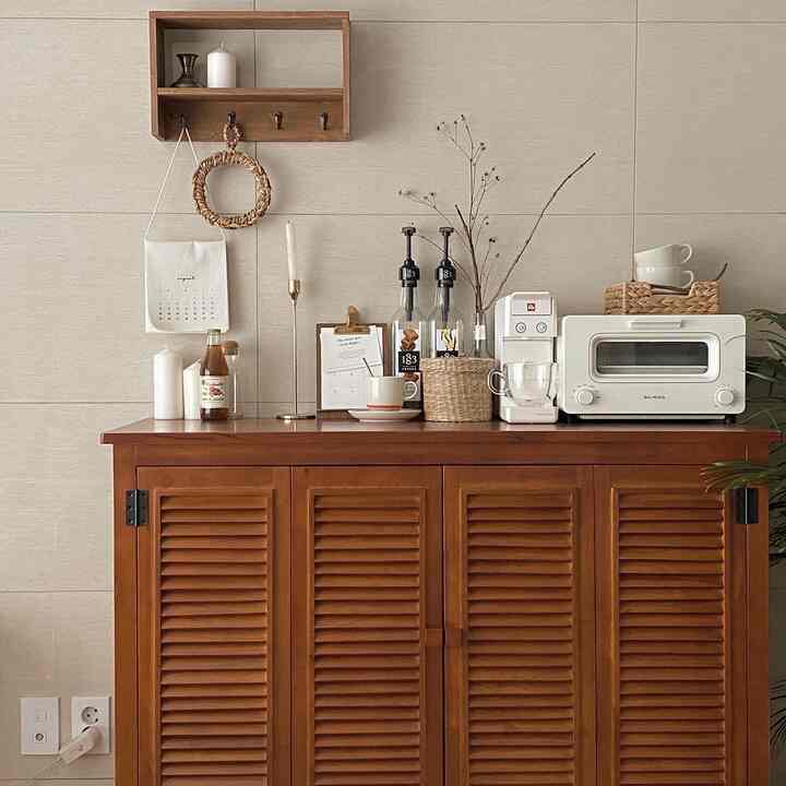 ベージュと木目調のキッチンスペース、天然木のキャビネットの上にコーヒー器具やキャンドル、カップが配置された雰囲気のあるインテリア