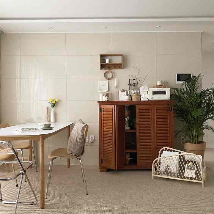 A natural dining room in ivory and wood tones, featuring a wooden dining table and chairs, louver cabinet, plants, and decorative items