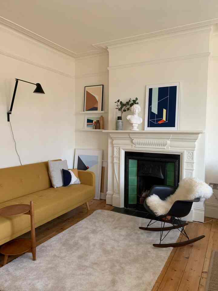 Nordic toned living room featuring a yellow sofa, light rug, wall art, and rocking armchair with minimal decor