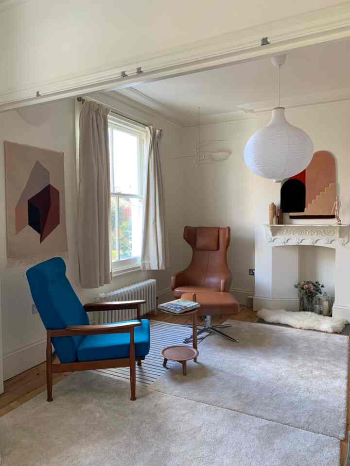 Modern living room with white walls and large rug, featuring blue and brown armchairs creating a cozy atmosphere