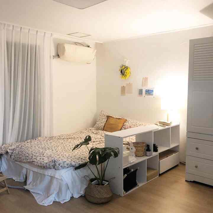 明るいホワイトトーンの居心地の良い寝室、花柄のベッドカバーと収納棚、自然素材の植物が配置された空間