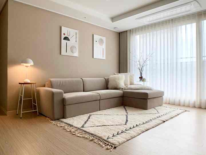 A beige and wood tone living room featuring a light brown L-shaped sofa, curtains, and rug, creating a harmonious natural modern interior