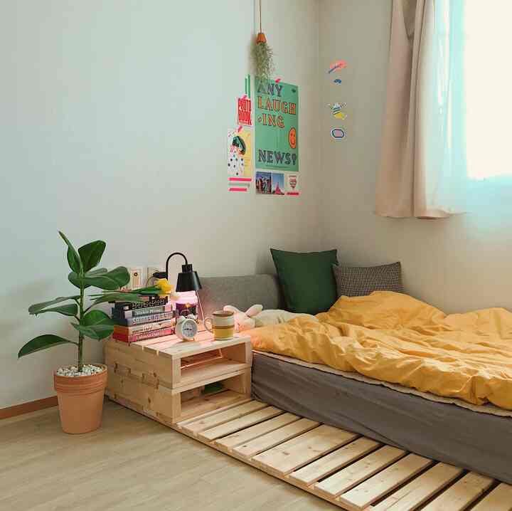 A cozy studio bedroom in yellow, beige, and gray tones featuring wood furniture and a plant, emitting warm energy