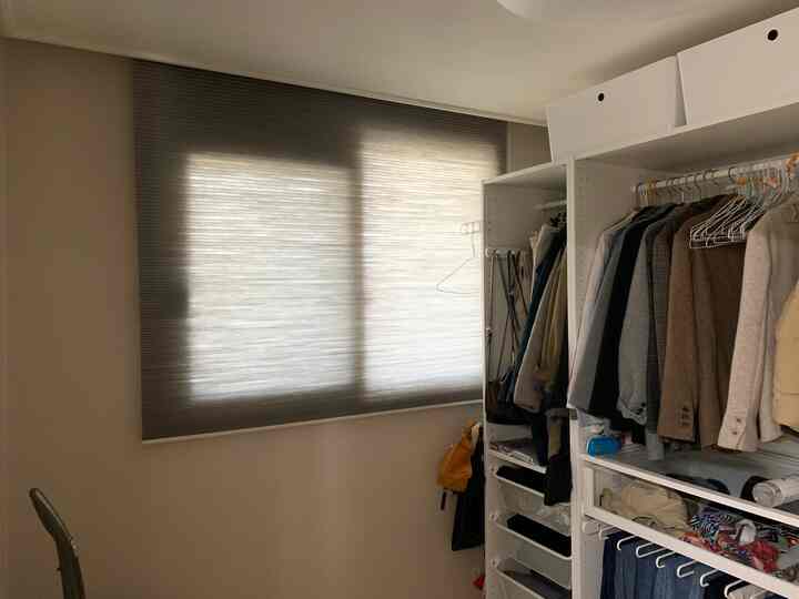 Bright and clean walk-in closet featuring natural wood tone blinds and white closet furniture