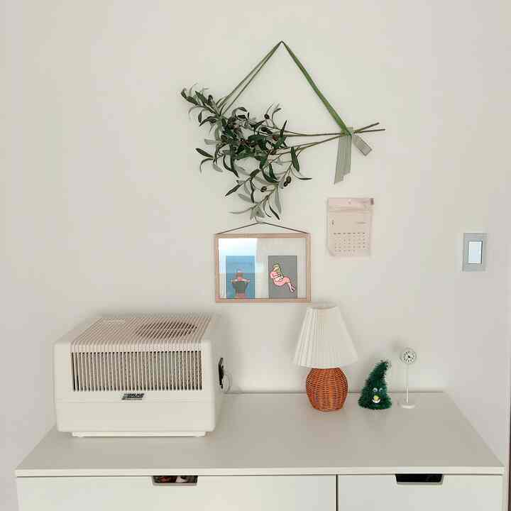 White-toned bedroom dresser topped with a humidifier, a mini lamp, and a small Christmas tree in a clean setting