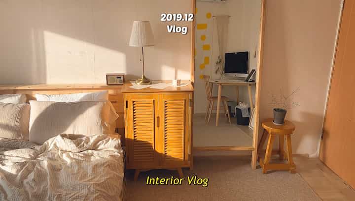 温かみのあるベージュと木目調の寝室、木製ナイトテーブルとスツールが配置されたナチュラルモダンな空間