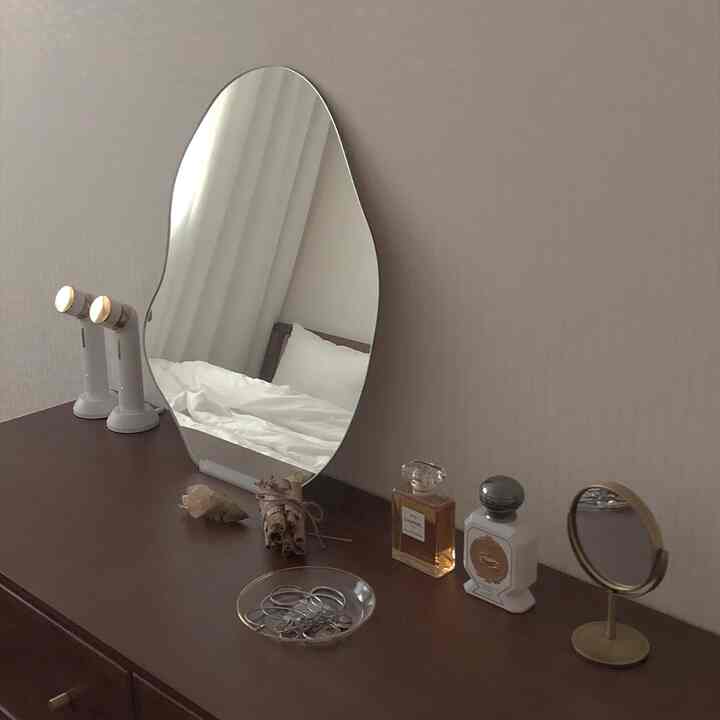 温かみのあるブラウン調の化粧台に、特徴的な形の鏡と香水、装飾品が配置された落ち着いたインテリア