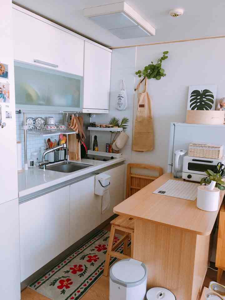 Natural modern studio kitchen in white and wood tones featuring a folding dining table and neatly arranged kitchen utensils, creating a cozy atmosphere