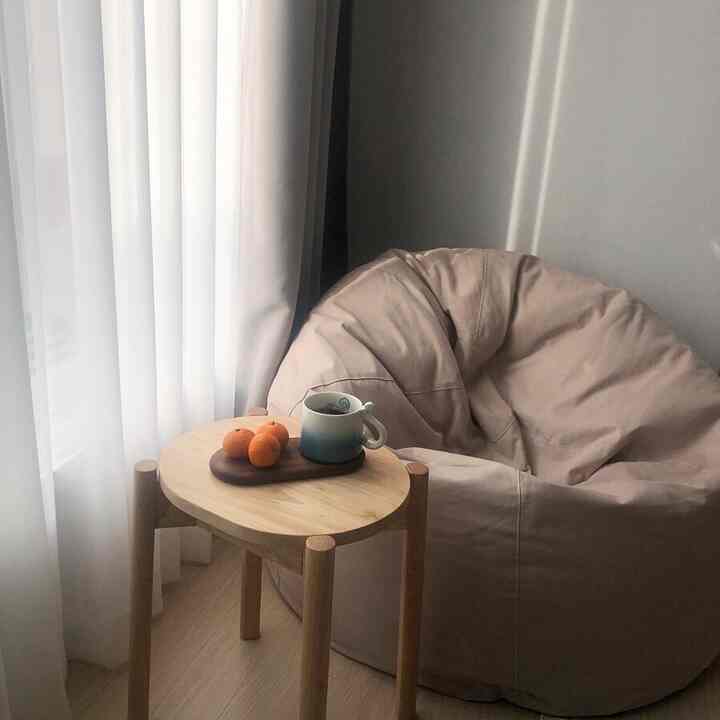 Cozy space featuring an ivory-beige bean bag and a small wood tone round table with soft white curtains
