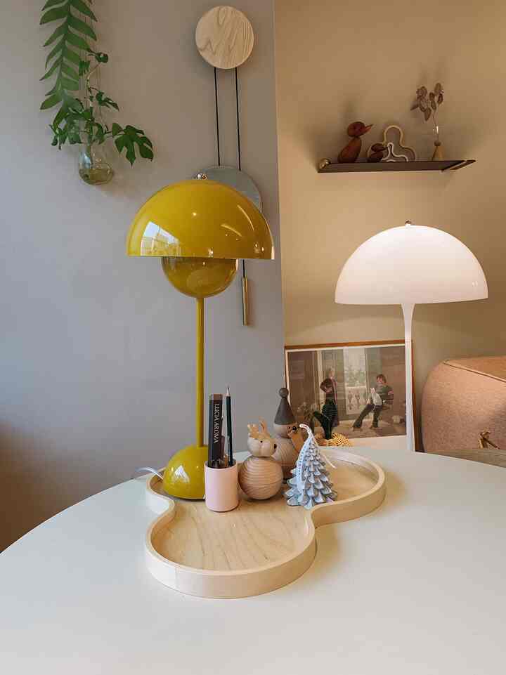 黄色と白のテーブルランプが置かれた丸い白いテーブルの上に木製トレイと飾りが配置されたナチュラルな雰囲気の空間