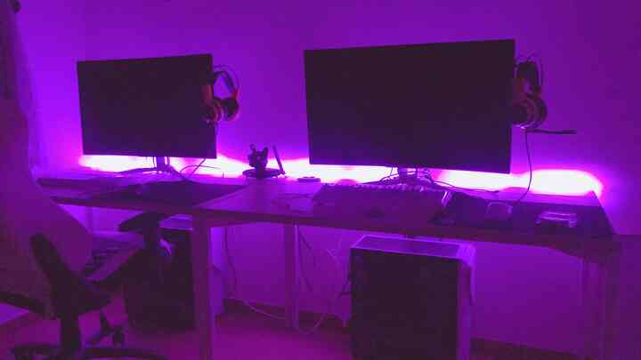 紫色のLED間接照明がある一人用のゲームルーム、デュアルモニターとゲーミングチェアが配置されたパソコンデスク空間