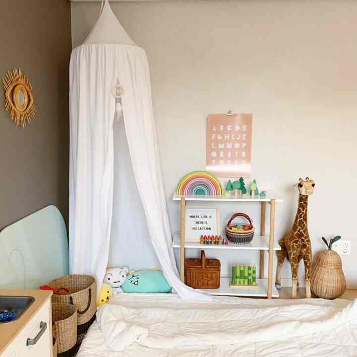 Natural beige tone kids' room featuring a white canopy, rattan baskets, and a toy shelf arranged charmingly