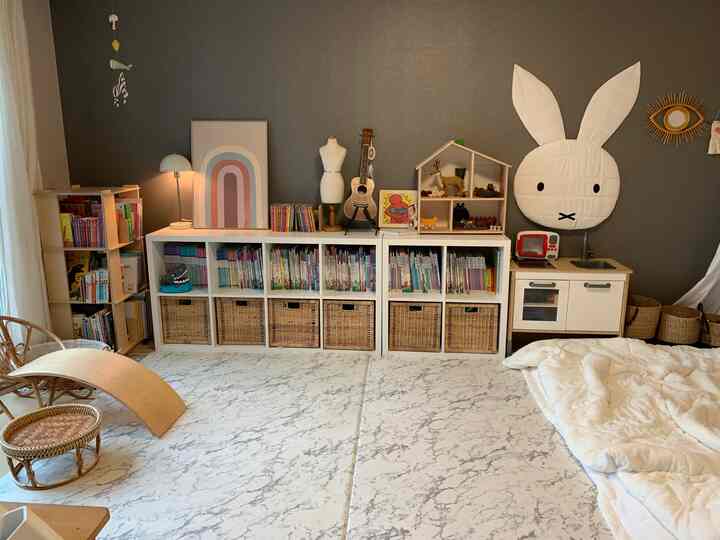 Gray wall kids' room featuring white bookshelves and rattan baskets with charming toys creating a cozy atmosphere