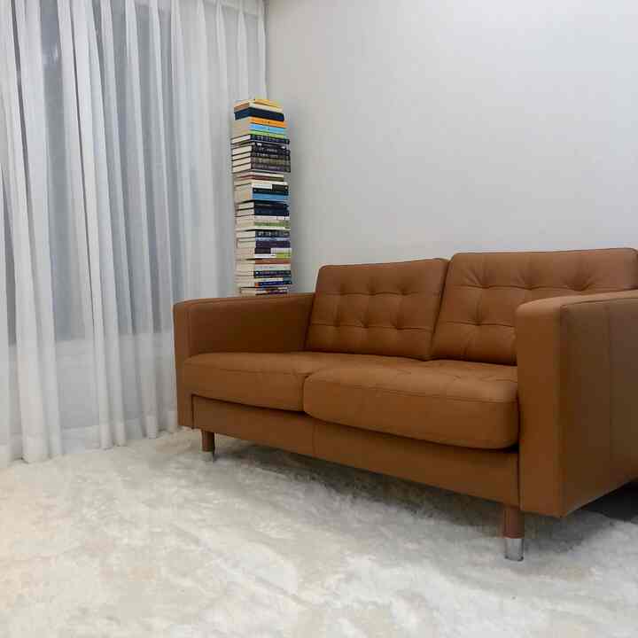 ナチュラルなブラウンのレザーソファと白いラグが配置されたシンプルなリビング