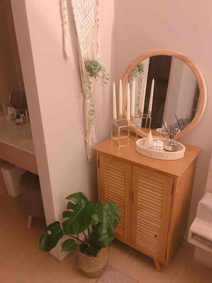 暖かい木目調とナチュラルな植物が配置された寝室のコーナー収納と丸い鏡が印象的な空間