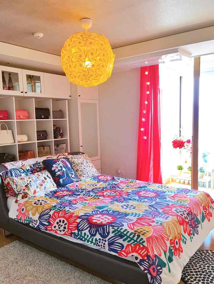 Bedroom with bright yellow pendant light, white walls, red curtains, and vivid multicolored floral bedding