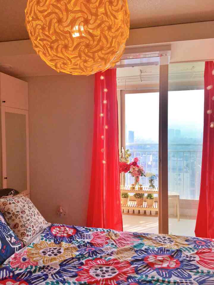 鮮やかな赤いカーテンと花柄の寝具が印象的な、窓とバルコニーのある明るく温かみのある寝室