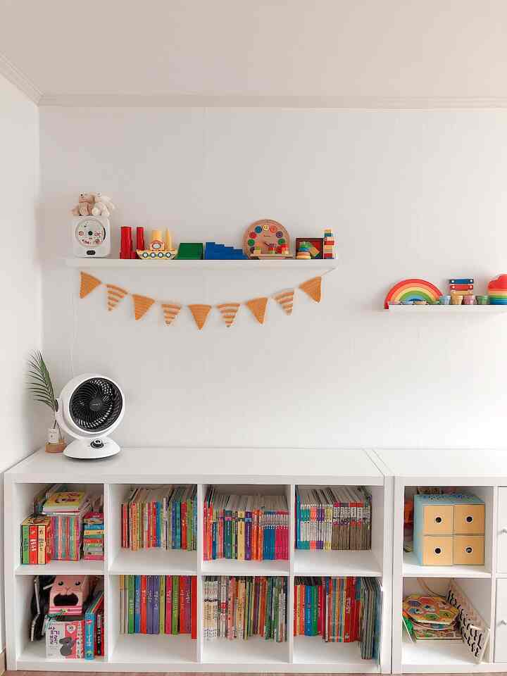 Bright white kids' room featuring white bookshelves filled with colorful children's toys and books, arranged neatly