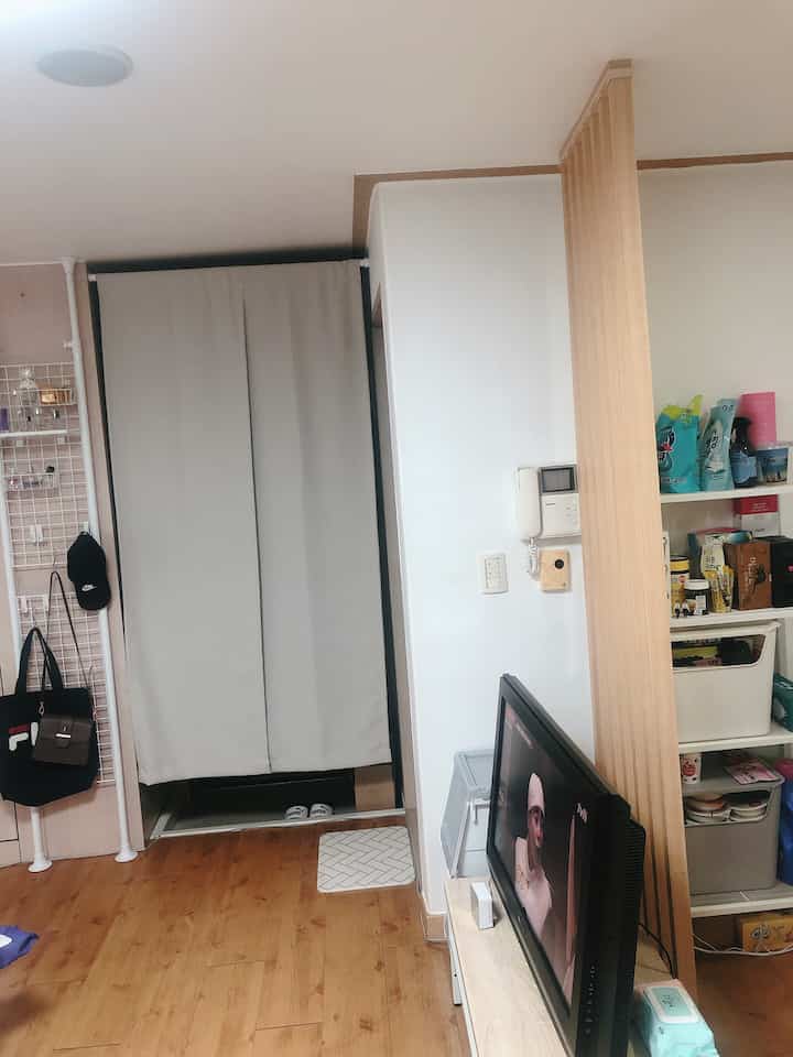Natural wood tones and light gray curtain in a small entrance area, featuring a wooden room divider and organized storage shelves in a typical interior