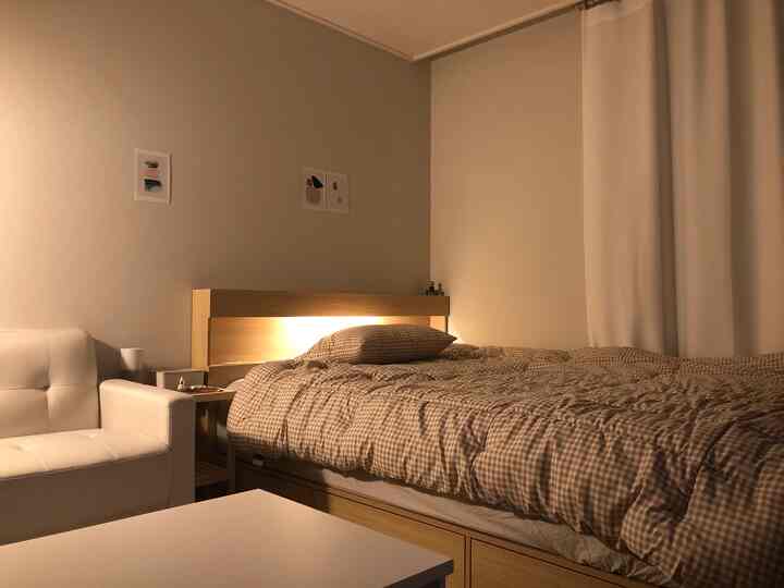 木目調と白を基調とした寝室、LED照明付き収納ベッドと白いソファが配置された落ち着いた空間