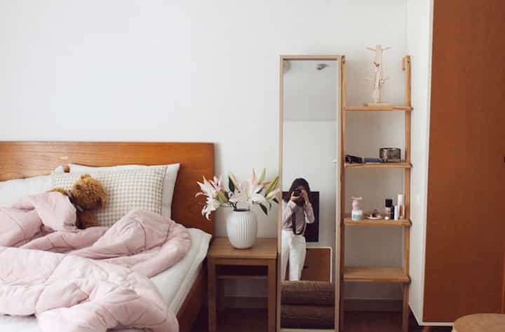 Bright white walls and natural wood tone furniture in a bedroom featuring pink bedding and a vase of lilies, creating a cozy atmosphere