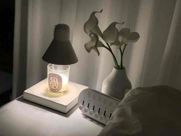 Cozy white-toned bedroom table featuring candle warmer and artificial calla lilies in a vase