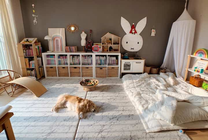 Cozy kids' room with gray wallpaper, white canopy, marble patterned play mat, pet dog resting, and children's toys neatly arranged