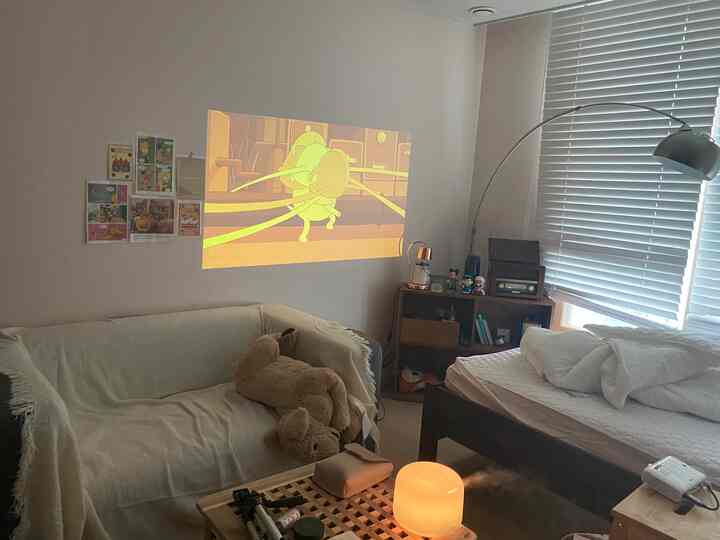 A white and brown toned student room featuring a sofa, bed, and projector creating a cozy atmosphere