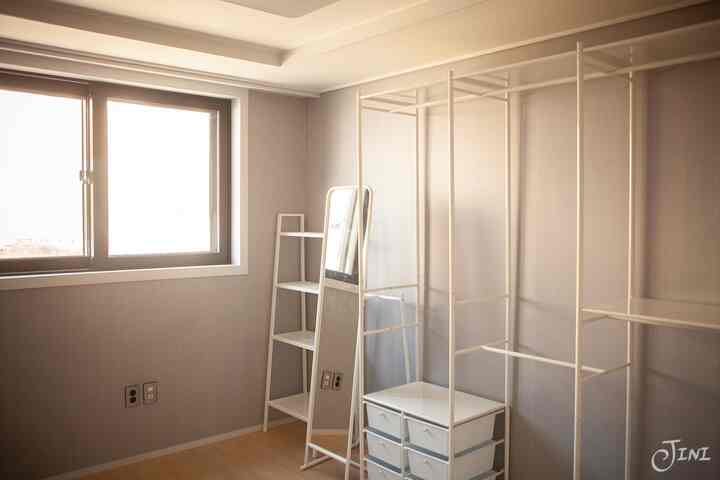 白い金属製の棚と全身鏡が配置されたナチュラルトーンのウォークインクローゼット、整然として実用的な収納空間