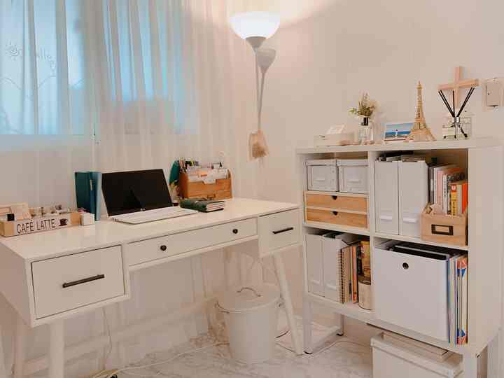 White-toned small room featuring a desk and organized storage shelf, creating a neat home office space