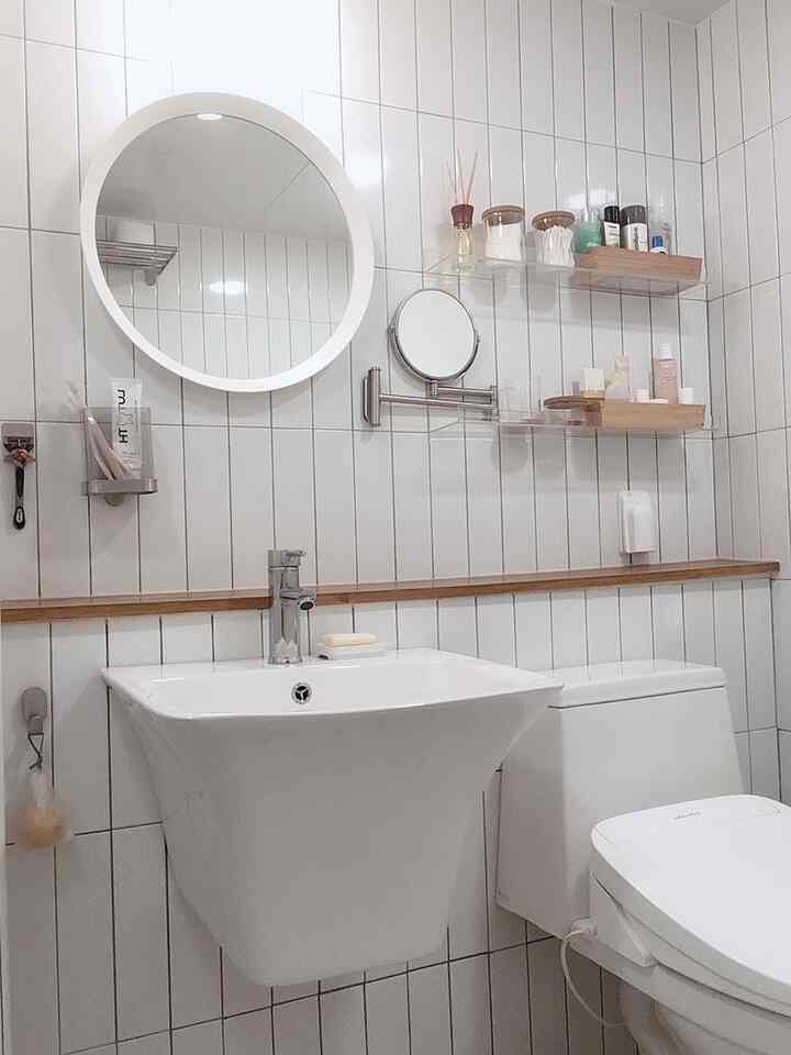 Clean bathroom interior with white tiles, transparent shelves, and round mirrors creating a simple look