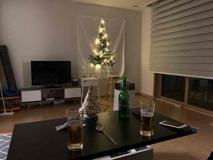 温かみのあるブラウンの床と白い壁の寝室、照明付きポスターとナイトテーブル、黒いコーヒーテーブルが配置された雰囲気のあるインテリア