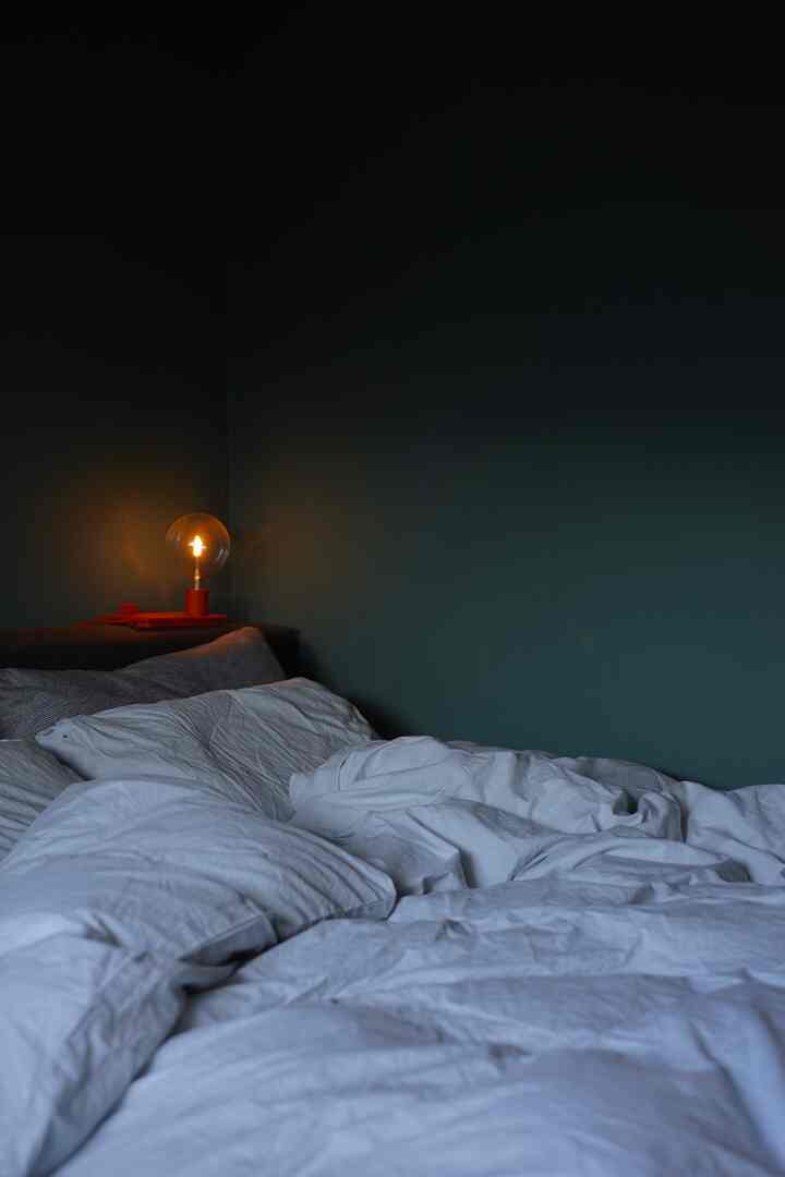 ダークグリーンの壁と白い寝具、オレンジのテーブルランプが配置されたモダンな寝室の雰囲気のあるインテリア