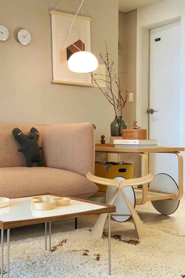 柔らかな木目調とグレーの壁が調和する北欧風リビング、ピンクのソファとペンダントライトが配置された温かみのある空間