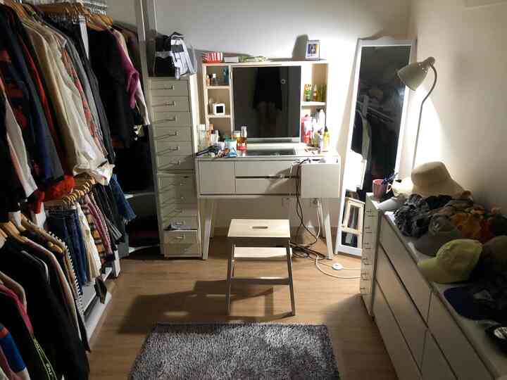 White and wood tone walk-in closet featuring a vanity desk with stool centrally arranged in a neat storage space