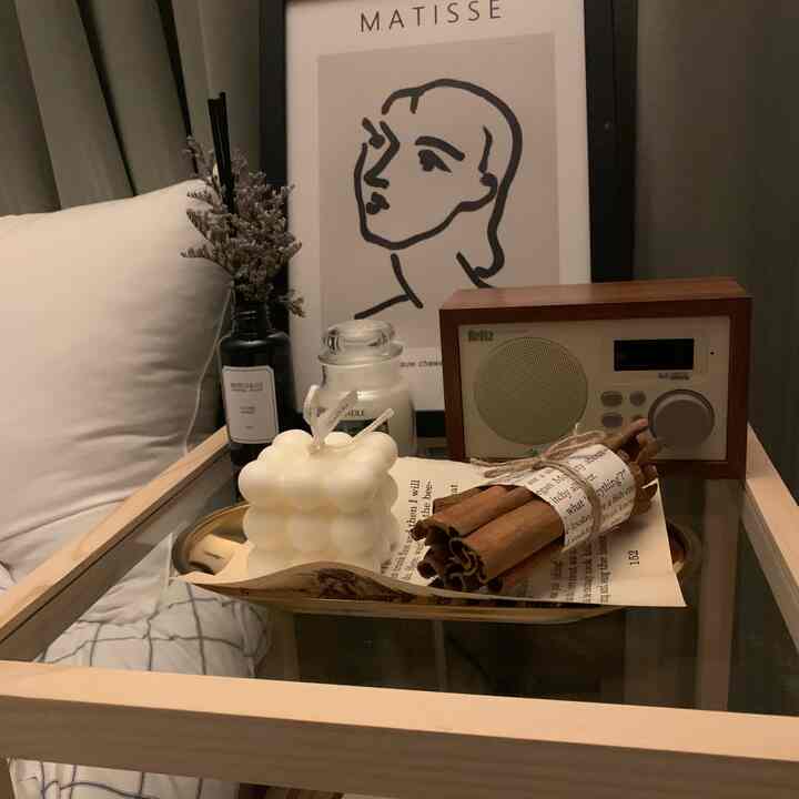 ナチュラルな木目調のサイドテーブルの上に、ヴィンテージスピーカーやキャンドル、ディフューザーが配置された居心地の良い寝室の一角