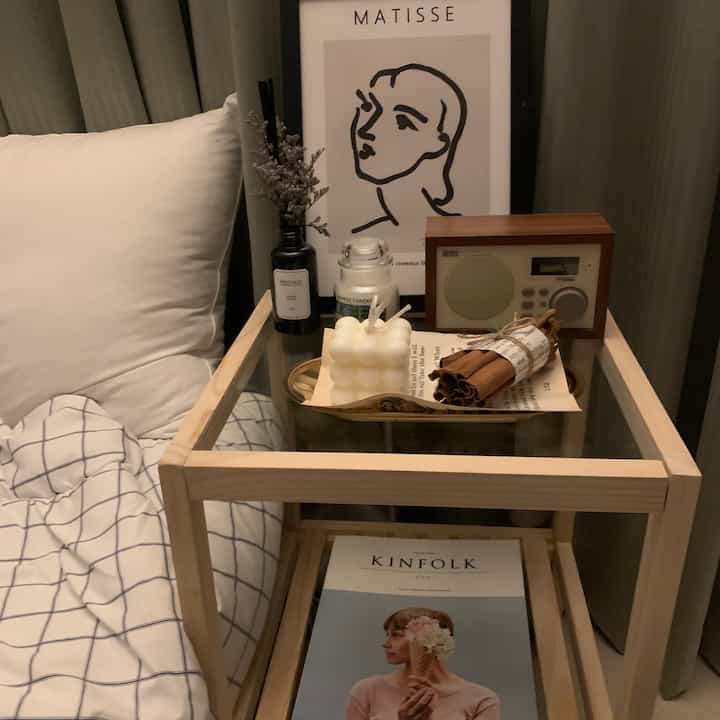 Cozy bedroom with bright wood tone nightstand and white bedding, warm atmosphere created by candles and poster