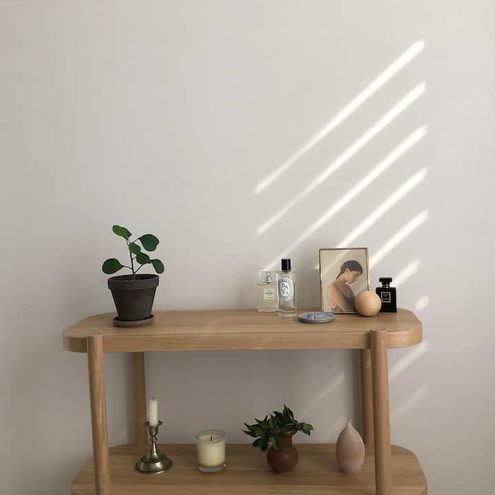 Minimal space featuring a wood tone console table with plant and diffusers on top, against a white wall