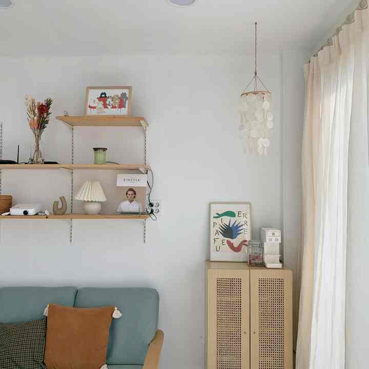 白い壁とベージュの木製棚、淡いブルーのソファが配置された温かみのある自然な印象のリビングルーム