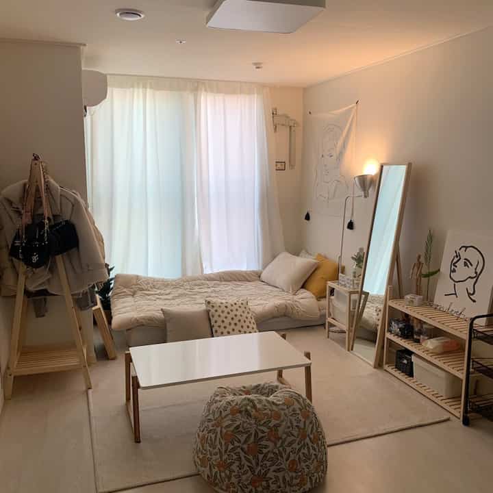 Soft ivory and wood-toned 8-pyeong studio featuring a low bed, full-length mirror, and shelves in a cozy single living space