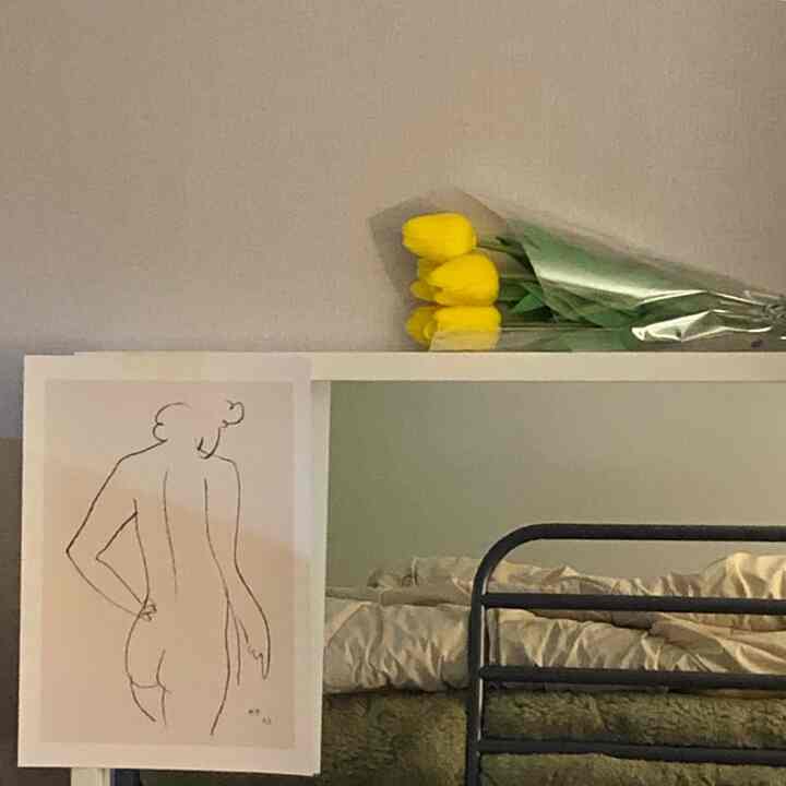 Natural-toned bedroom with white walls and bed frame, featuring a mirror and yellow tulip decoration as focal points