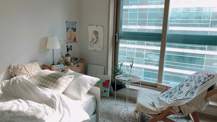 White and beige toned studio bedroom featuring an armchair and coffee table by the window for a cozy relaxation space