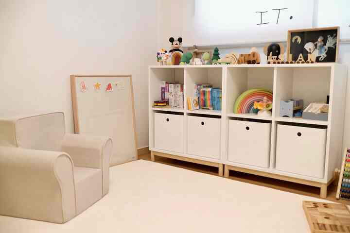A simple and natural baby room featuring white and wood tones, with a kids' chair and toy storage unit arranged neatly