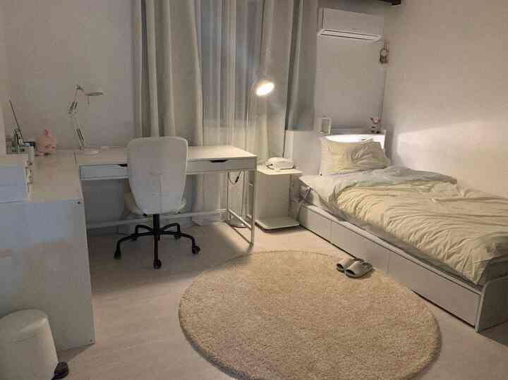 ホワイトトーンのワンルーム寝室、机やベッドが配置されたシンプルで清潔感のある空間